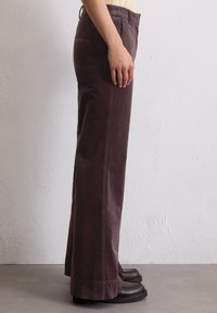 Bruine corduroy wijde broek met zijzakken, gestructureerde stof en een relaxte pasvorm, gedragen met zwarte hoge hakken.