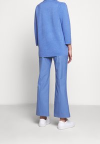 Ljusblå tröja med trekvartsärmar, i kombination med matchande vida byxor och vita sneakers. Slät textur, avslappnad passform.