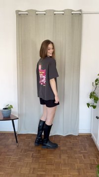 Grå t-shirt med en färgglad blommig grafik, tillsammans med svarta shorts och knähöga svarta stövlar. Bakgrunden har ett ljust draperi.