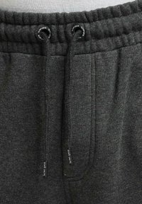Mørkegrå sweatpants fremstillet af tekstureret stof, med en elastisk talje og snøre, samt synlige mærke-tags ved lommerne.