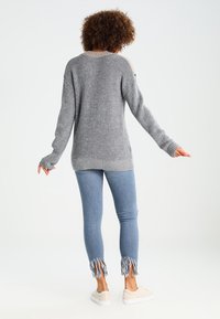 Grauer Strickpullover mit lockerer Passform, langen Ärmeln und gerippten Bündchen, kombiniert mit hellblauen Jeans mit fransigen Säumen und beigen Sneakern.