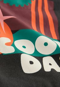 Textil mit schwarzem Hintergrund und mehrfarbigen Grafiken: orangefarbenen, türkisfarbenen und weißen Buchstaben und Mustern, einschließlich Pflanzen- und Zahnradmotiven.