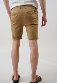 Shorts beiges en tissu doux, avec des revers aux ourlets, deux poches arrière et une petite étiquette de marque sur la taille.
