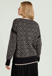Czarny i kremowy sweter dziergany z geometrycznym wzorem, ściągaczami na mankietach i u dołu oraz luźnym krojem. Posiada kontrastujący pas na rękawach.