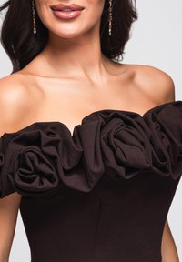 Schulterfreies Kleid aus dunkelbraunem Stoff mit einem Rüschensaum am Ausschnitt, der rosenähnliche Falten bildet, und einer figurbetonten Silhouette.