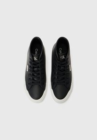 Sneakers neri realizzati in materiale liscio con suole in gomma bianca. Presentano un classico design con lacci e un logo stampato sulla linguetta.