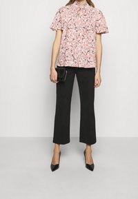 Blůza s květinovým vzorem v růžové barvě, krátké rukávy a nařasený výstřih, doplněná černými zkrácenými kalhotami a černými špičatými podpatky.