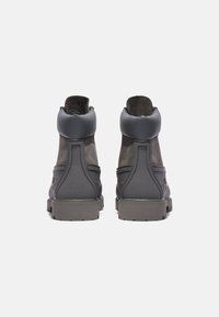 Bottines montantes grises avec une finition texturée, un panneau mat contrastant, un col rembourré et des semelles en caoutchouc robustes. Pas de marquage ni de motifs visibles.