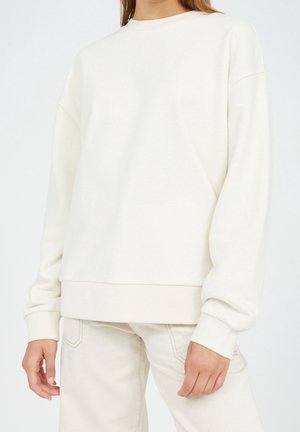 Sweatshirt couleur crème en tissu doux, avec des manches longues, un col rond et une coupe décontractée. Poignets et ourlet sans coutures.