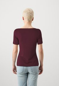 Burgunderfarget topp med korte ermer og vid hals, figurnær design og glatt tekstur, kombinert med lyseblå jeans. Minimal detaljering.