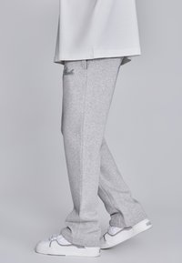 Pelēki sporta bikses ar brīvu piegriezumu un sānu kabatām, ar melnu izšūtu logotipu uz augšstilba un mīkstu, teksturētu audumu.