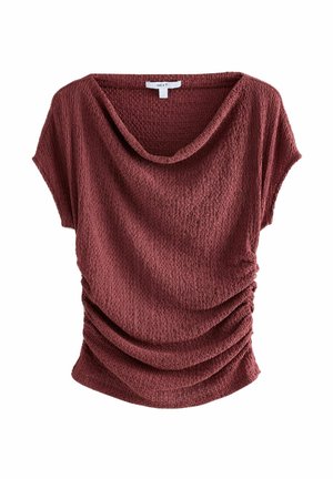 Haut rouge à manches courtes avec un col drapé et un tissu texturé, présentant des détails froncés sur les côtés pour plus de dimension.