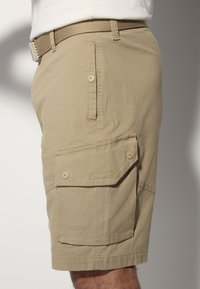 Beige cargo shorts with a textured finish, featuring two side pockets with button closures and a buttoned back pocket. Belt included.
