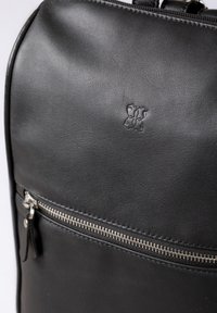 Black leather backpack featuring a smooth texture, a front zipper pocket with metallic hardware, and an embossed logo detail.