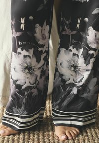 Pantalonii negri cu flori au flori mari albe și gri cu accente verzi. Marginea are un design în dungi alb-negru. Piciorul este vizibil.
