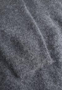 Grå tekstureret stof med fine, bløde fibre. Materialet fremstår fuzzy og tykt, hvilket viser en tættere vinkel på tekstilets overflade.