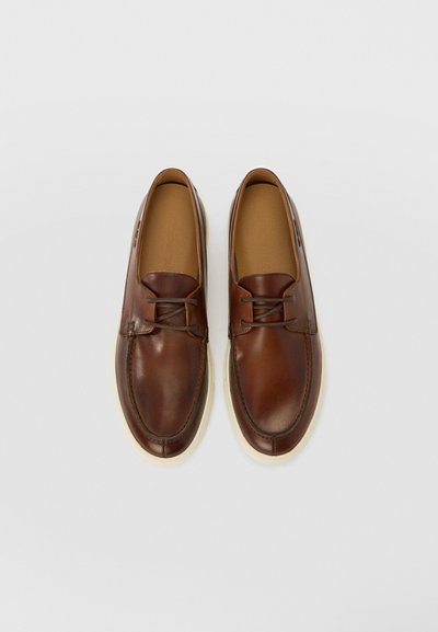 Brown leather shoes with a rounded toe, lace-up design, and tan interior. Features a contrasting white rubber sole and stitching accents.