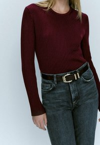 Bordowy, prążkowany top z długim rękawem zestawiony z ciemnymi dżinsami i brązowym paskiem z złotą klamrą. Gładka tekstura, dopasowany krój.