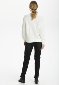 Biały sweter dzianinowy z teksturowanym wzorem i ściągaczami przy mankietach, zestawiony z czarnymi dopasowanymi dżinsami i botkami za kostkę. Widoczne detale na plecach.