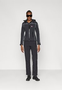 Jaqueta desportiva preta com detalhes cinzentos, frente com fecho de correr, capuz e dois bolsos laterais, combinada com calças e sapatilhas pretas.