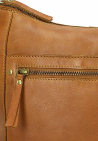 Primo piano di una borsa in pelle marrone con una tasca con zip, hardware in ottone e cuciture a contrasto, dal texture liscia e finitura morbida.