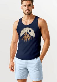 Navy tank top featuring a mountain graphic in beige with trees and birds. Paired with light blue shorts, made of soft fabric.