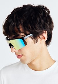 Sonnenbrille mit einem schwarzen Rahmen, großen blauen Gläsern und einem umschließenden Design, das einen schlanken Nasensteg und ein glänzendes Finish aufweist.