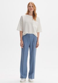 T-shirt blanc à manches courtes en tissu texturé avec une coupe décontractée, agrémenté d'une poche, associé à un pantalon large taille haute bleu clair et à des baskets blanches.