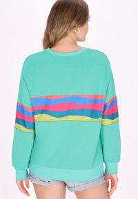 Heller türkisfarbener Sweatshirt mit bunten horizontalen Streifen in Pink, Blau und Gelb. Mit langen Ärmeln und einer lässigen Passform. Weicher Textur.