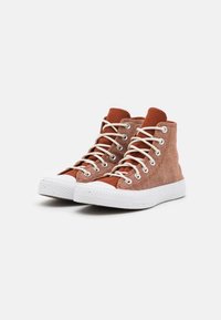 Zapatillas altas de material de lona marrón rojizo, concordones blancos y suelas de goma con acentos texturizados.