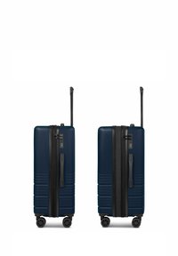 Valise rigide bleu marine avec finition texturée, deux poignées latérales et un trolley rétractable. Équipée de quatre roues pivotantes pour une mobilité optimale.
