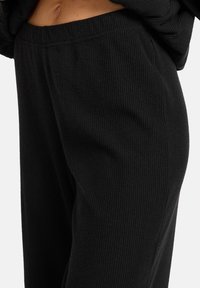 Zwarte geribde loungebroek met een elastische tailleband, voorzien van een zachte textuur en een relaxte pasvorm, met verticale ribpatronen.