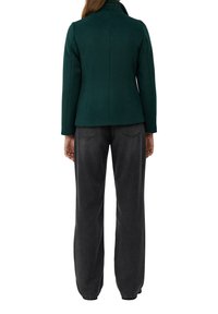 Grüne Wollmischung Jacke mit tailliertem Schnitt, hohem Kragen und langen Ärmeln, kombiniert mit schwarzen, weiten Jeanshosen.