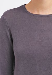 Grå stickad tröja med rund halsringning, långa ärmar och en mjuk textur. Tyget verkar mjukt och lätt, utan mönster eller dekorationer.