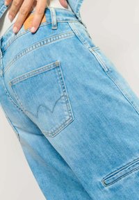 Lichtblauwe denim jeans met een zichtbare achterzak met een gestikt ontwerp. Het materiaal heeft een zachte textuur en lichte vervaging. Leren label op de tailleband.