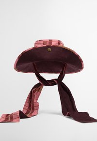 Chapéu de abas largas em veludo cor-de-rosa com o interior estampado e um detalhe de lenço em bordeaux amarrado na base. Apresenta um acabamento metálico.