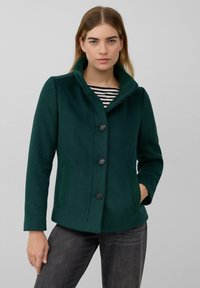 Dunkelgrüner Wollmischjacke mit fünf Knöpfen, übergroßem Kragen und gerippten Seitentaschen. Trägt man über einem schwarz-weißen gestreiften Oberteil.
