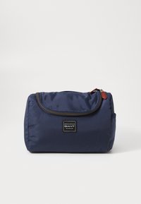 Navy blå polstret toalettmappe med glidelås, rektangulær form, en lærdetalj og et merke på forsiden.