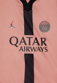 Jersey de color rosa claro con un diseño de escote en V negro. Presenta "QATAR AIRWAYS" en letras negras en negrita, un acento negro y el logo de Jordan.