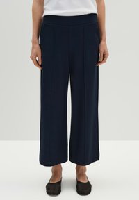 Marineblauwe wijde broek met een gestructureerd patroon, elastische tailleband en zijnaaddetails. Gecombineerd met zwarte instappers.