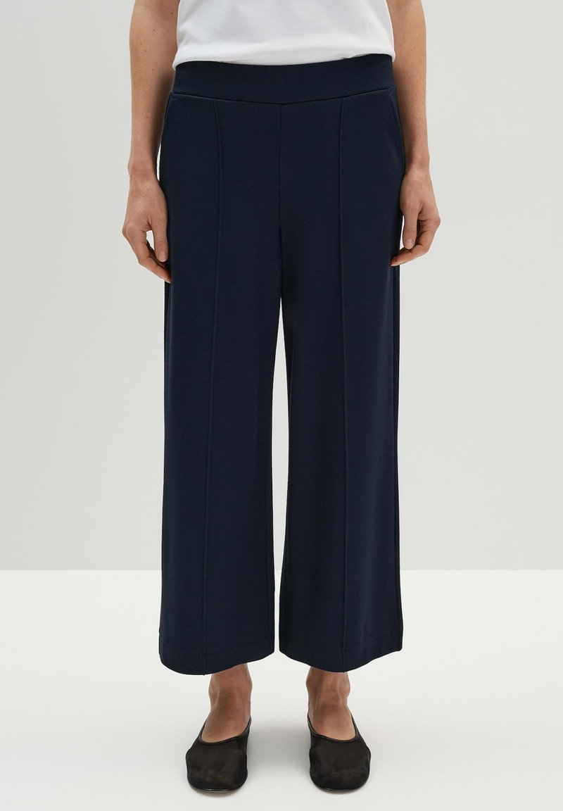 Marineblauwe wijde broek met een gestructureerd patroon, elastische tailleband en zijnaaddetails. Gecombineerd met zwarte instappers.