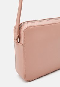 Różowa skórzana torebka na ramię o prostokątnym kształcie, zamknięciu na suwak i cienkim pasku. Gładka faktura z widocznymi detalami przeszyć.