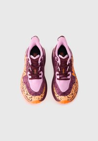 Chaussures de sport violettes et roses avec une tige texturée, un embout blanc et une semelle orange et noire. Elles présentent des lacets ton sur ton et des accents de marque.