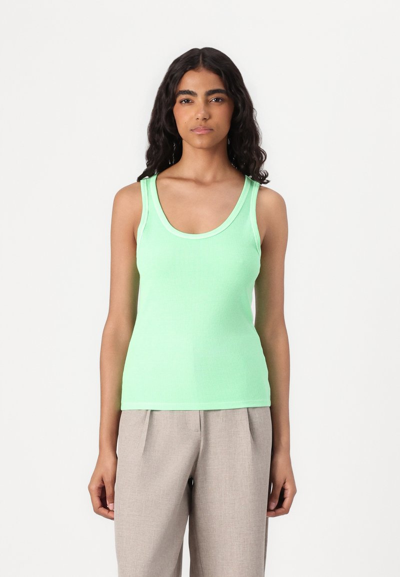 Light green ribbed tank top with a scoop neckline and narrow shoulder straps. Paired with light gray pleated trousers, creating a casual look.
