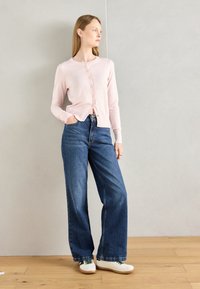 Light pink cardigan with round neckline and button closure, paired with high-waisted wide-leg blue denim jeans and white sneakers.