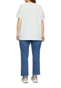 Witte katoenen t-shirt met korte mouwen, gecombineerd met blauwe denim broek. Zichtbare sneakers met een gaasontwerp en grijze accenten.