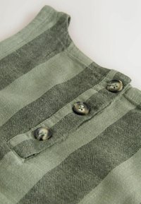 Prim-plan al unei țesături verzi cu dungi verticale largi și trei nasturi multicolori cusuti pe o pată.