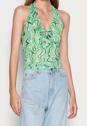 Femme portant un haut dos-nu à motif ondulé vert et blanc avec un détail anneau sur le devant et un jean taille haute bleu clair.