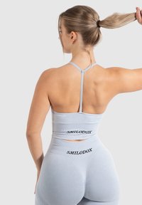 Top deportivo azul claro con tirantes finos y un detalle con corte, acompañado de leggings de cintura alta que presentan una marca negra en la parte posterior.