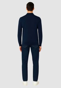 Polo shirt a maniche lunghe blu scuro con colletto, slim fit, abbinato a jeans scuri e sneakers bianche, visto da dietro.